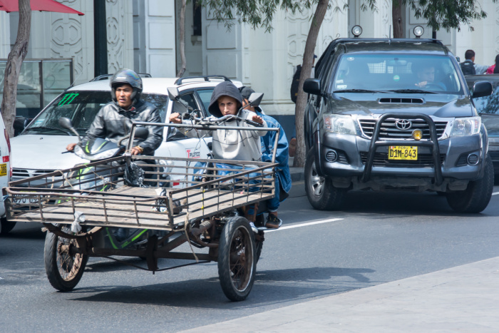 Klasický paradox Limy: Motorová tříkolka prodírající se ulicemi mezi novými vozy